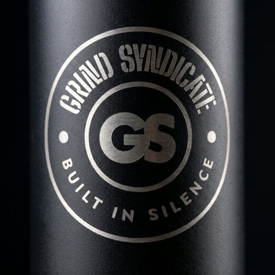 Close-up of the laser-etched Grind Syndicate GS badge on the matte black bottle, reading Built in Silence