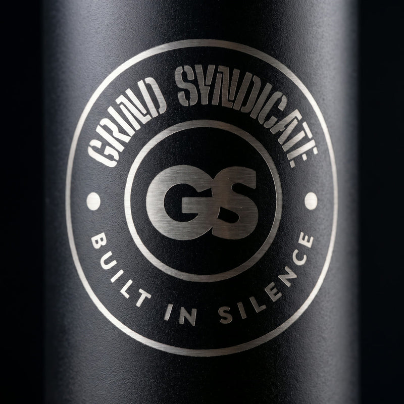 Close-up of the laser-etched Grind Syndicate GS badge on the matte black bottle, reading Built in Silence