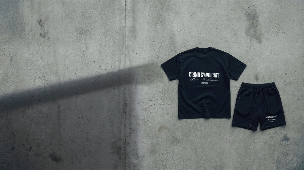The Origin Tee shown from the back and the Origin Shorts from the front, both Jet Black, laid out on concrete